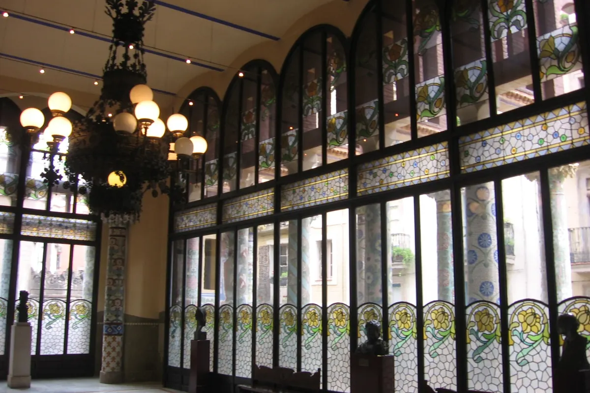 The Sala Lluís Millet, a tall salon with a wall of arched stained-glass windows and a large hanging lamp.